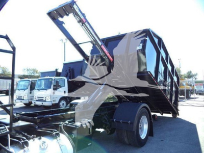 Peterbilt 337 roll-off truck with hydraulic lift arm and empty dump bed, side view showing rear dual tires and chassis.