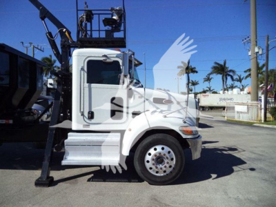 Peterbilt 337 roll-off truck side view showing cab with white paint and front wheel, hydraulic lifting equipment in background.