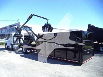 Peterbilt 337 rolloff truck with a black dump body in a lot, loading crane and white cab visible.