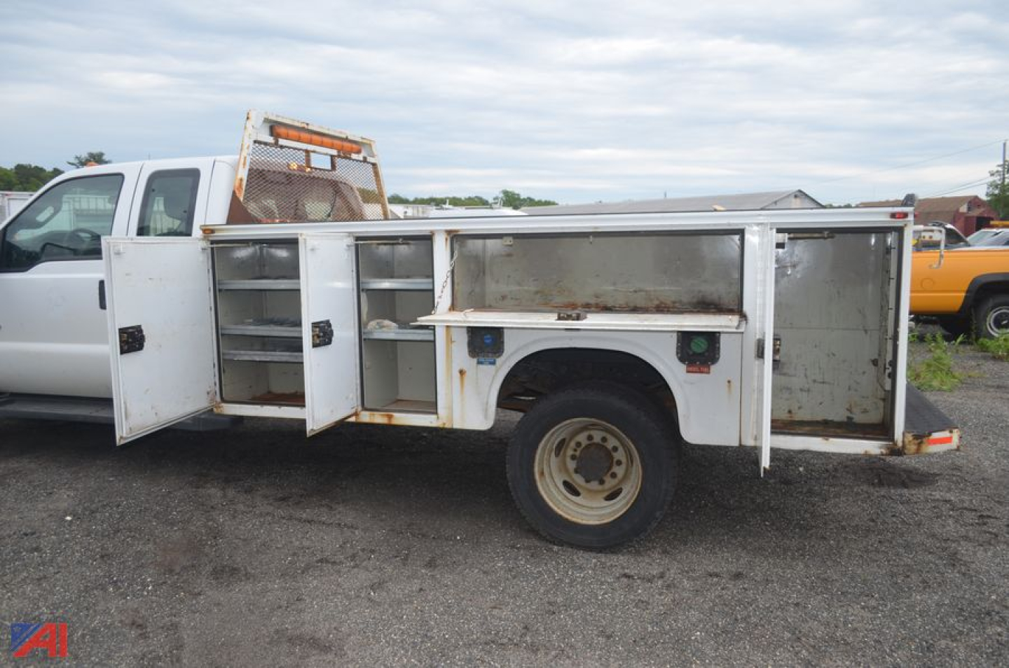 Ford F-550 utility truck bed showing multiple metal compartments with open doors and tool racks, single rear wheel, white paint with wear, and a tilted ladder rack at the front.