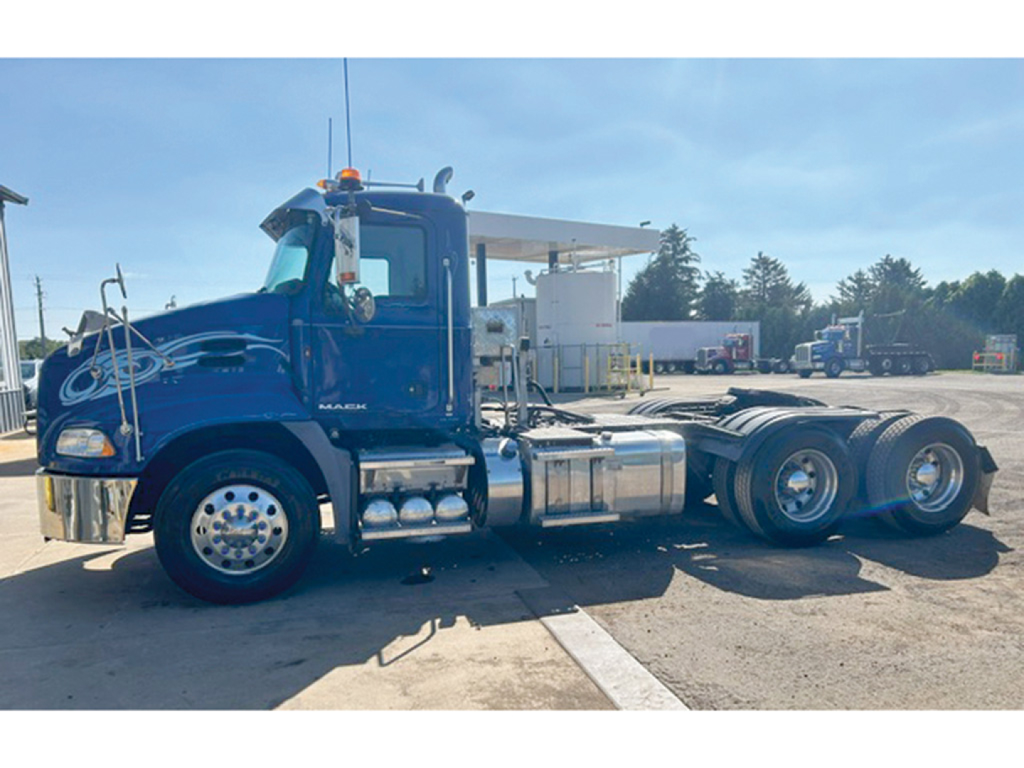Blue 2014 Mack CXU613 daycab tractor in service showing chrome fuel tanks and rear triple axle configuration.