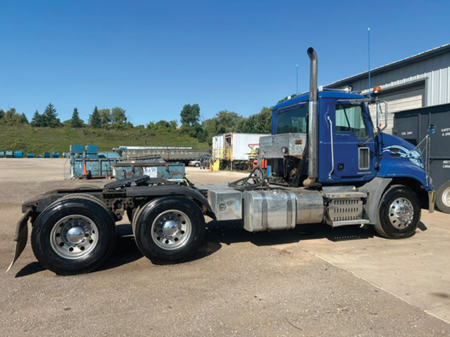 Blue 2014 Mack CXU613 daycab tractor chassis with dual rear axles and tall exhaust stack, side view showing fuel tanks and chassis components.