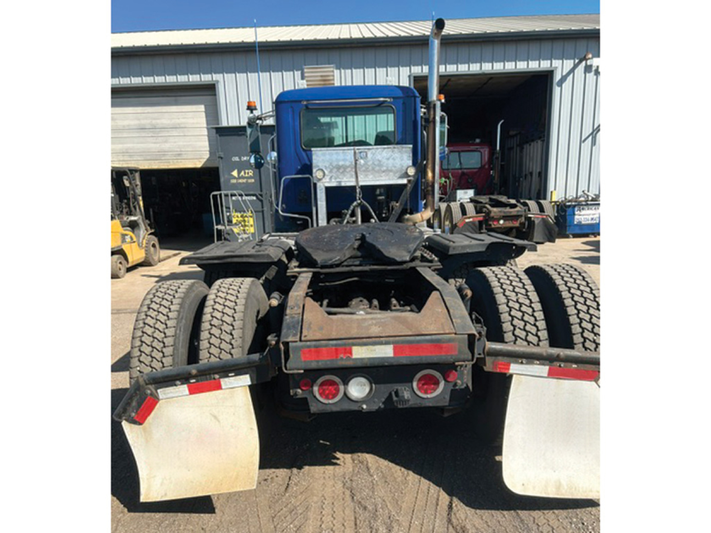 Truck rear view of a 2014 Mack CXU613 tractor showing dual rear axles, fifth wheel, and mud flaps in a yard.