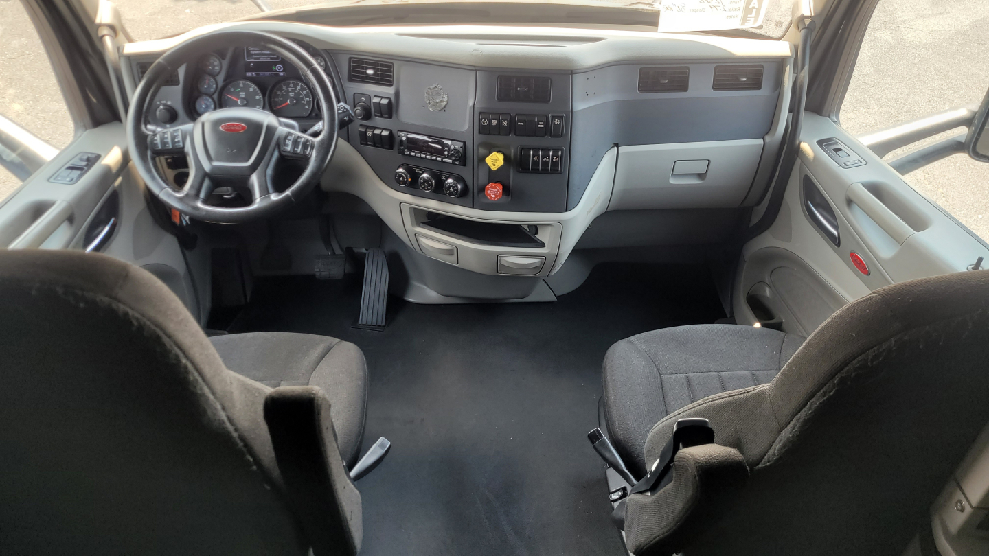 Peterbilt 579 interior cab dash and steering wheel view from passenger seat showing dashboard controls, steering wheel, and driver/passenger seats.