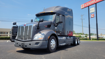 Peterbilt 579 conventional sleeper truck in a dealership lot, front-left view with chrome grille, large headlamps, and dual rear axles.