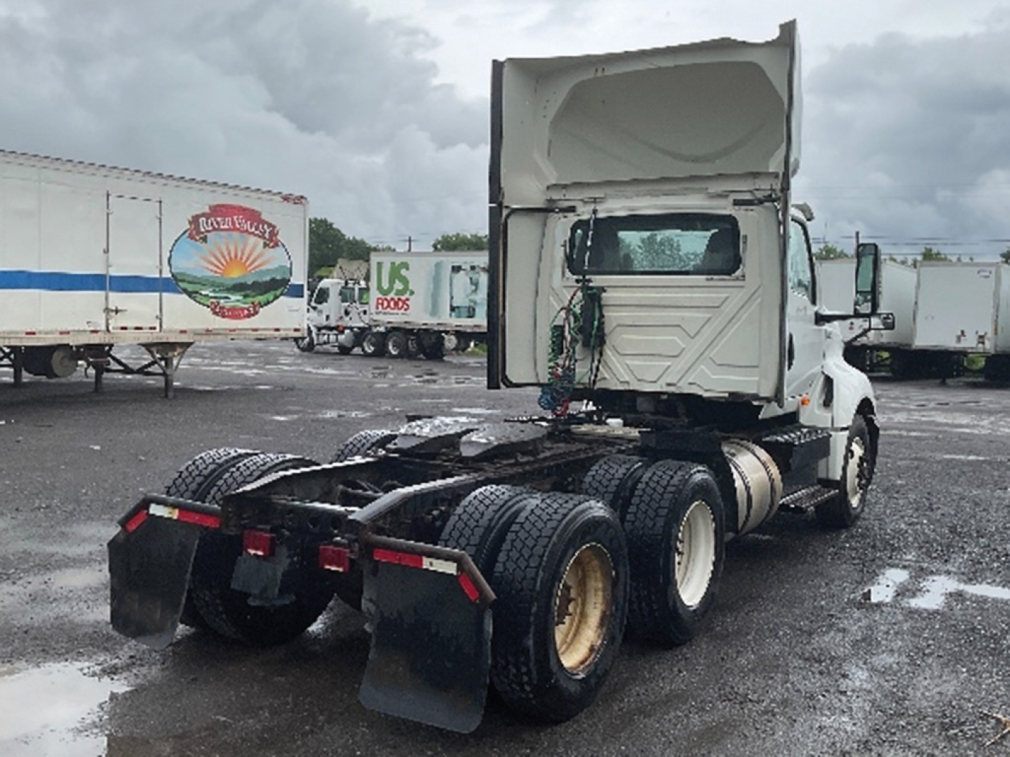 Truck chassis of a 2019 International LT625 tractor in a truck yard, rear view showing fifth wheel, dual rear axles, and mud flaps.