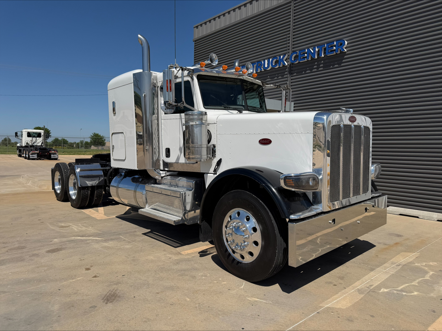 Peterbilt 389 conventional sleeper truck in white, side view with chrome bumper and exhaust stacks, near a building labeled TRUCK CENTER.