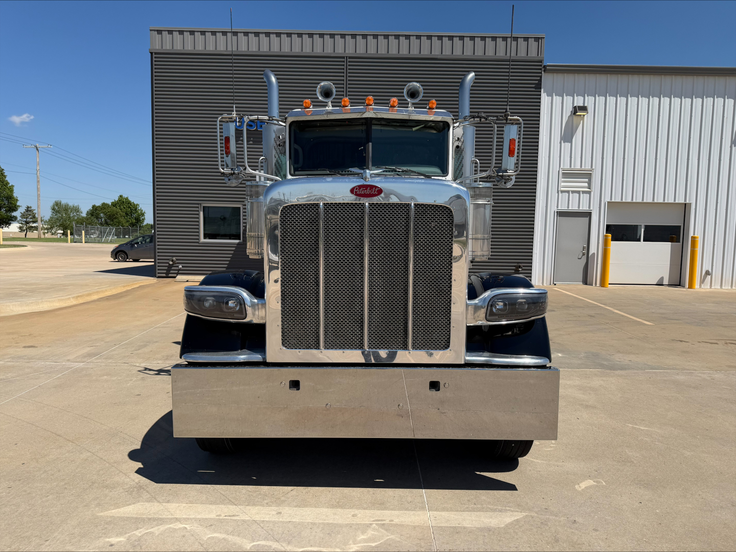 Peterbilt 389 head-on view showing large chrome grille, dual air intakes, and bumper; front badges and small text on the truck are visible but not legible from distance.