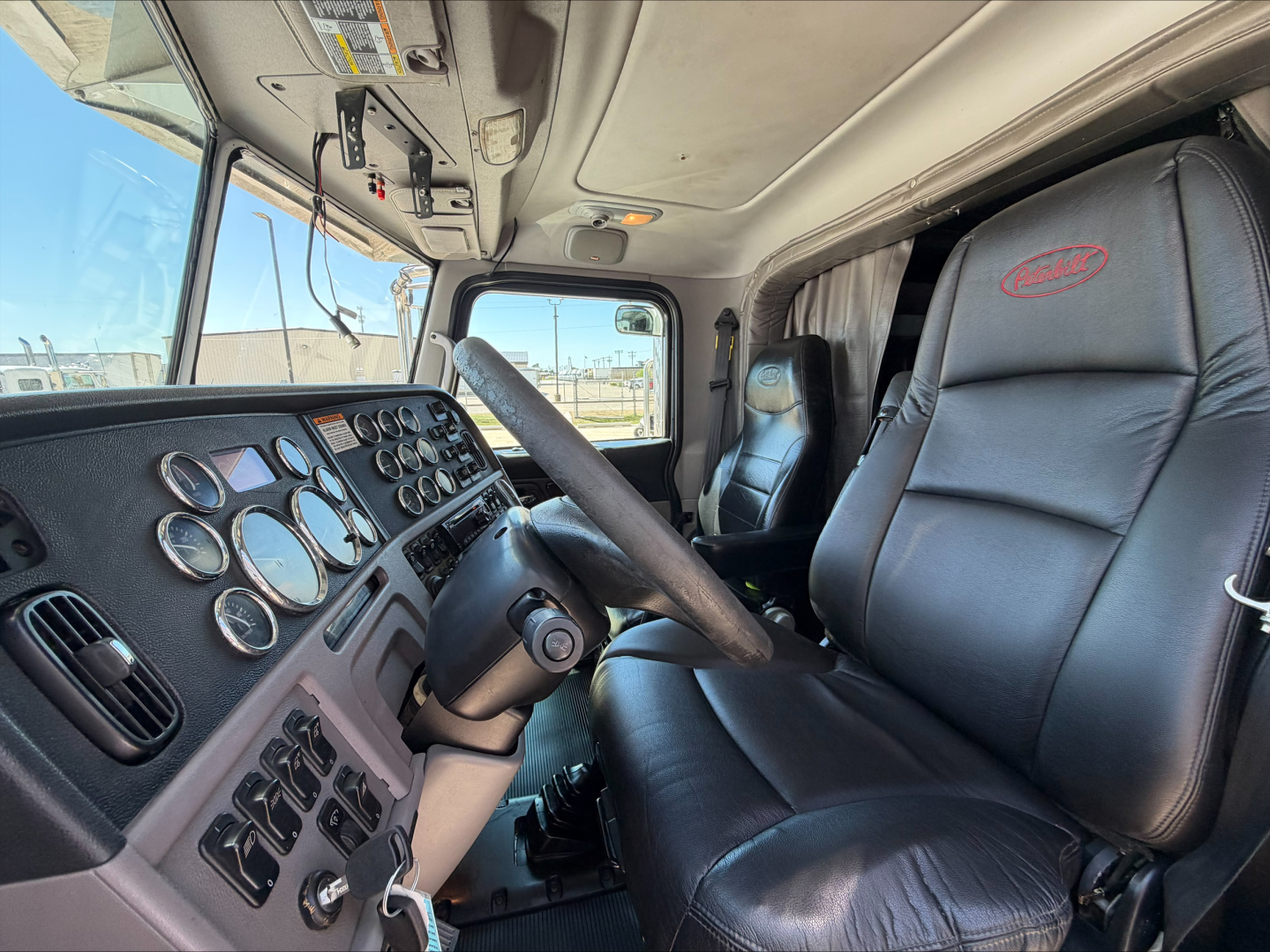 Peterbilt 389 truck interior showing steering wheel, instrument cluster, and driver's seat with Peterbilt logo on headrest.