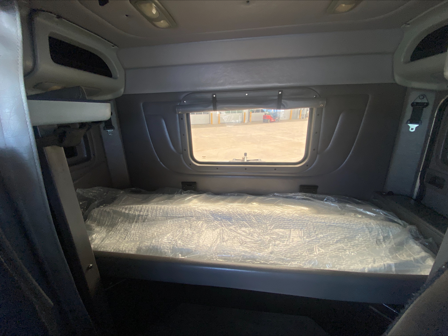 Peterbilt 389 sleeper cab interior featuring a side window bunk area with plastic-covered mattress and overhead cabinets.