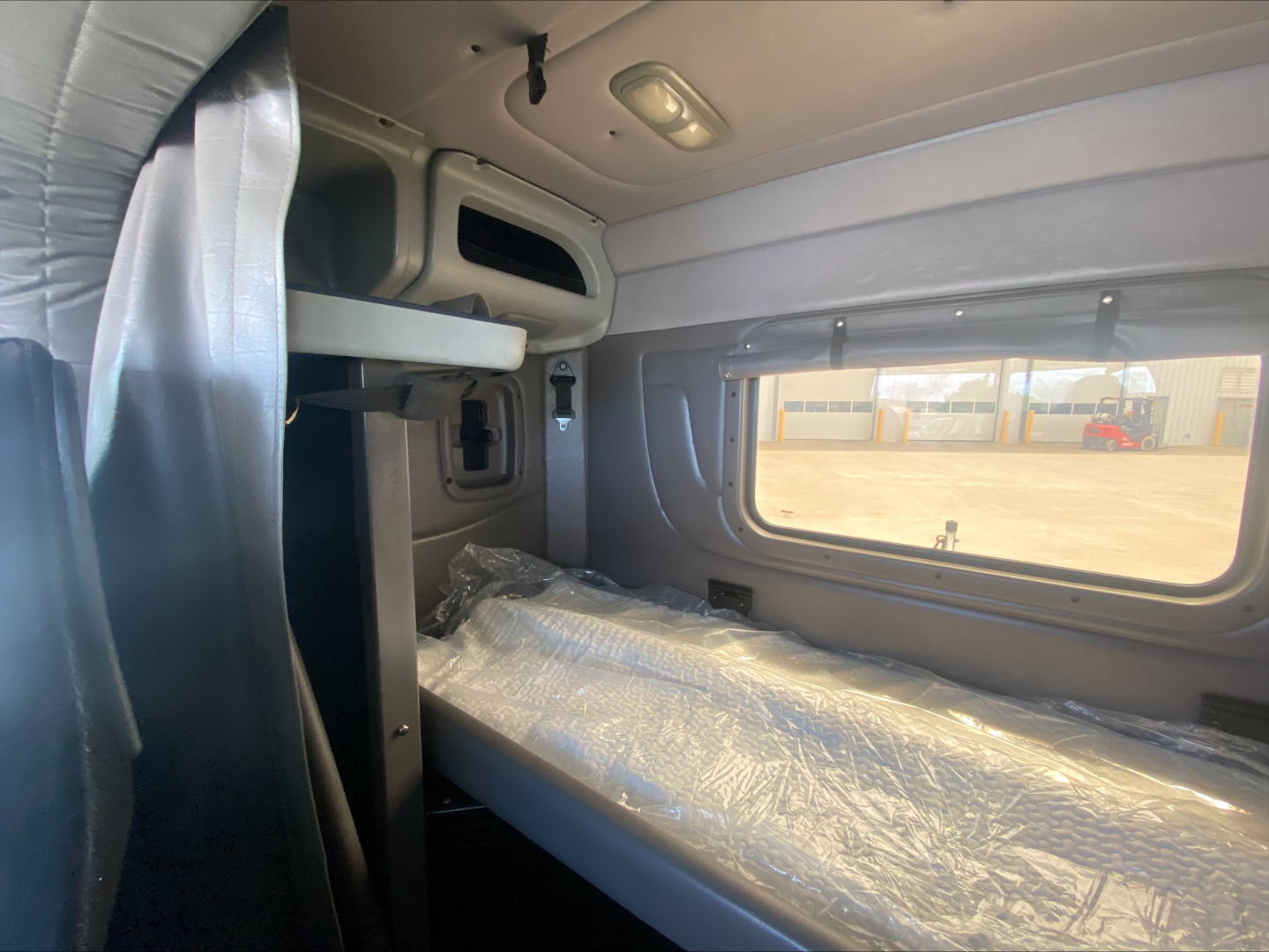 Peterbilt 389 sleeper cab interior showing bunk bed with plastic cover and window view.