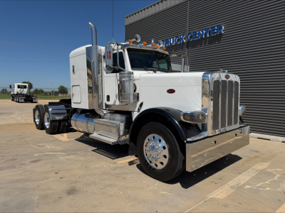 Peterbilt 389 conventional sleeper truck in white, side view with chrome bumper and exhaust stacks, near a building labeled TRUCK CENTER.