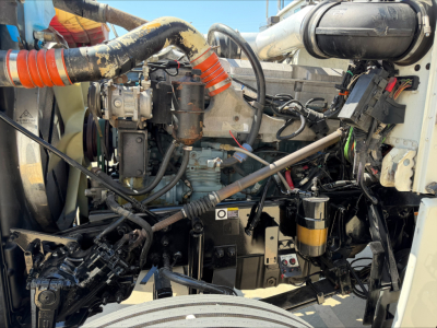 Peterbilt 389 engine bay showing diesel engine components, hoses, wiring, and auxiliary filters in the front compartment.