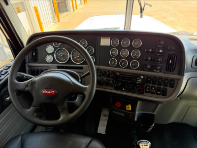 Peterbilt 389 interior dashboard and steering wheel with multiple gauges and controls visible.