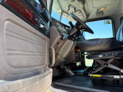 Interior of a Peterbilt 389 cab showing steering wheel, driver seat, pedals, and dashboard from a low angle.