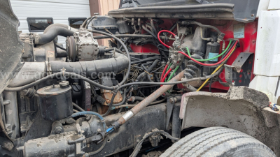Truck engine bay with various hoses, wires, and components visible; includes intake piping, battery area, and red body panels.