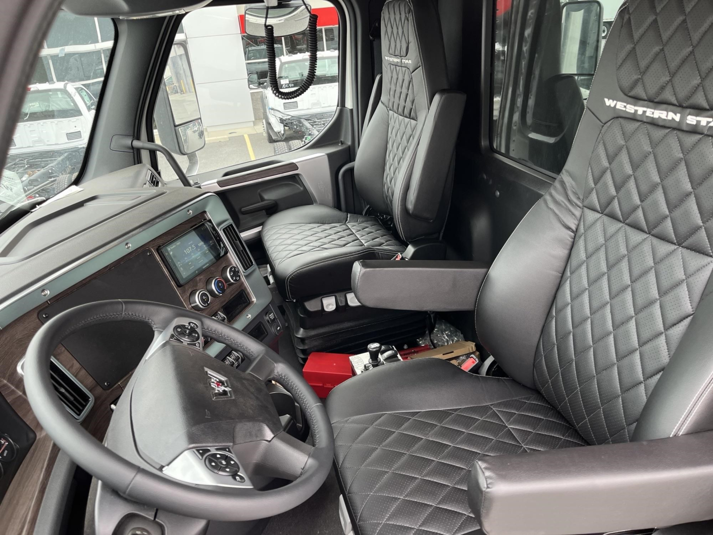 Interior of a Western Star truck cab with diamond-stitched seats, steering wheel, and dashboard; visible are control panel, central touchscreen, and gear selector. Passenger seat shows Western Star logo on headrest.