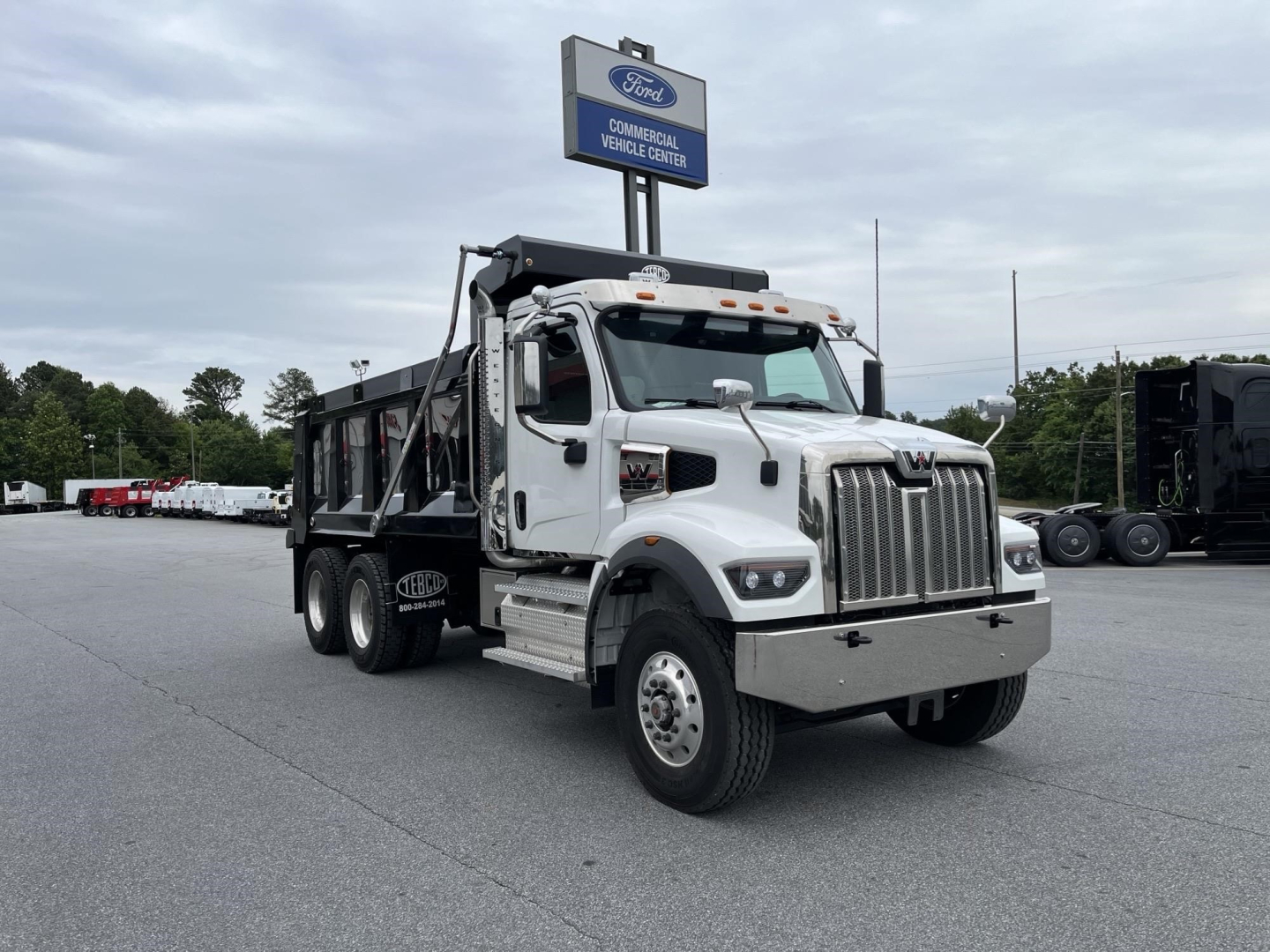 Dump truck in a dealership lot, 2027 Western Star 47X, white cab, black dump body, front grille, stock number 342827 visible.