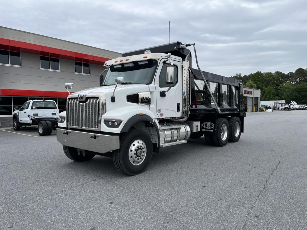 Western Star 47X dump truck in showroom lot, white cab, black dump body, front grille, chrome bumper, large daytime running lights, side mirrors, dual rear axles, VIN sticker visible