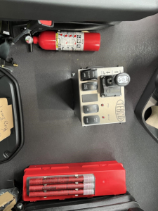 Cab interior of a Western Star 47X showing a red fire extinguisher, a TEG or DEF control panel, and a red tool case with multiple screwdrivers. Visible labels on extinguisher and control unit.