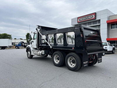 Dump truck chassis and cargo bed of a new Western Star 47X with black dump body, white cab, dual rear axles, parked in a dealership lot.