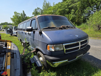 Dodge Ram Van cargo van from 1997 in blue, front and side view, overgrown grass around wheel wells, windshield with wipers, headlights, and grille visible.