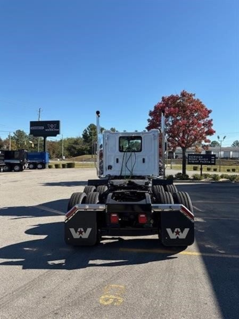 Rear view of a 2026 Western Star 49X Day Cab truck in a dealership lot showing dual rear axles and spare wheels with white cab.