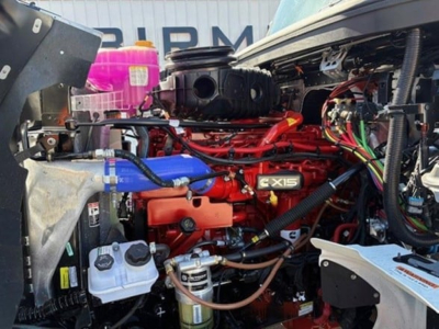 Truck engine bay with red CX15 engine and various hoses and wiring visible; blue coolant hose, white reservoir, and metal components in foreground.