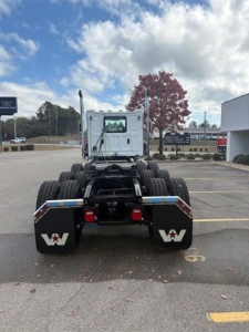 Rear view of a new Western Star 49X day cab tractor in a parking lot showing dual rear axles, mud flaps with Western Star logo, and fifth wheel area.