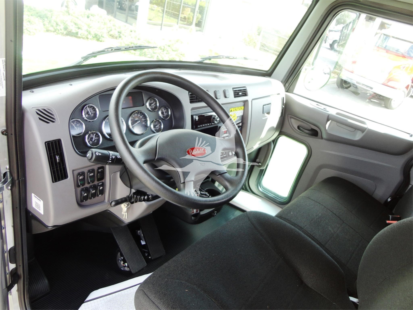 Peterbilt 337 cab interior showing steering wheel and dashboard gauges, driver seat, and entry area with pedals and controls.