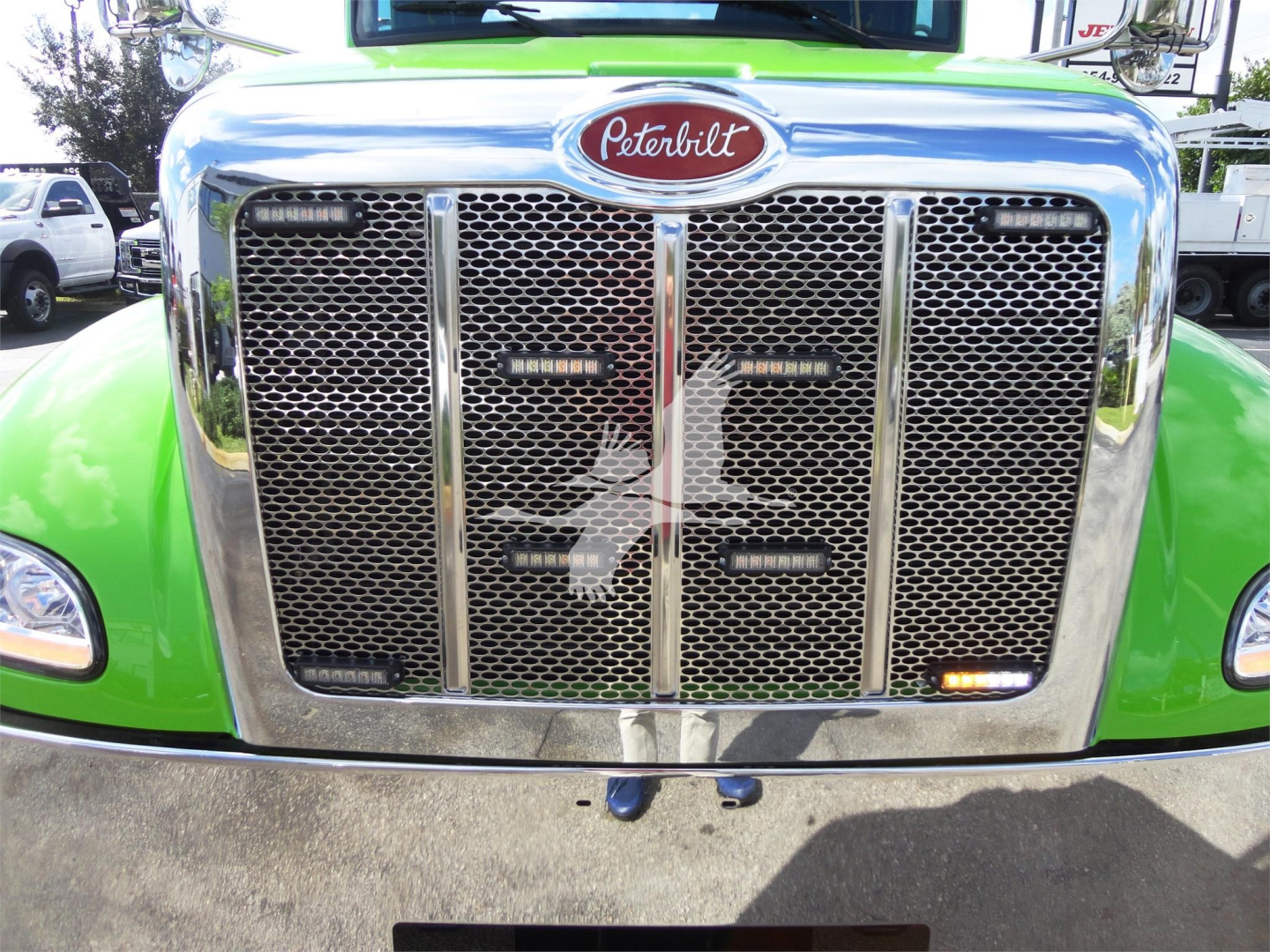 Peterbilt 337 front grille with chrome surround and Peterbilt emblem, green cab visible on sides, large mesh grille and bumper with reflection