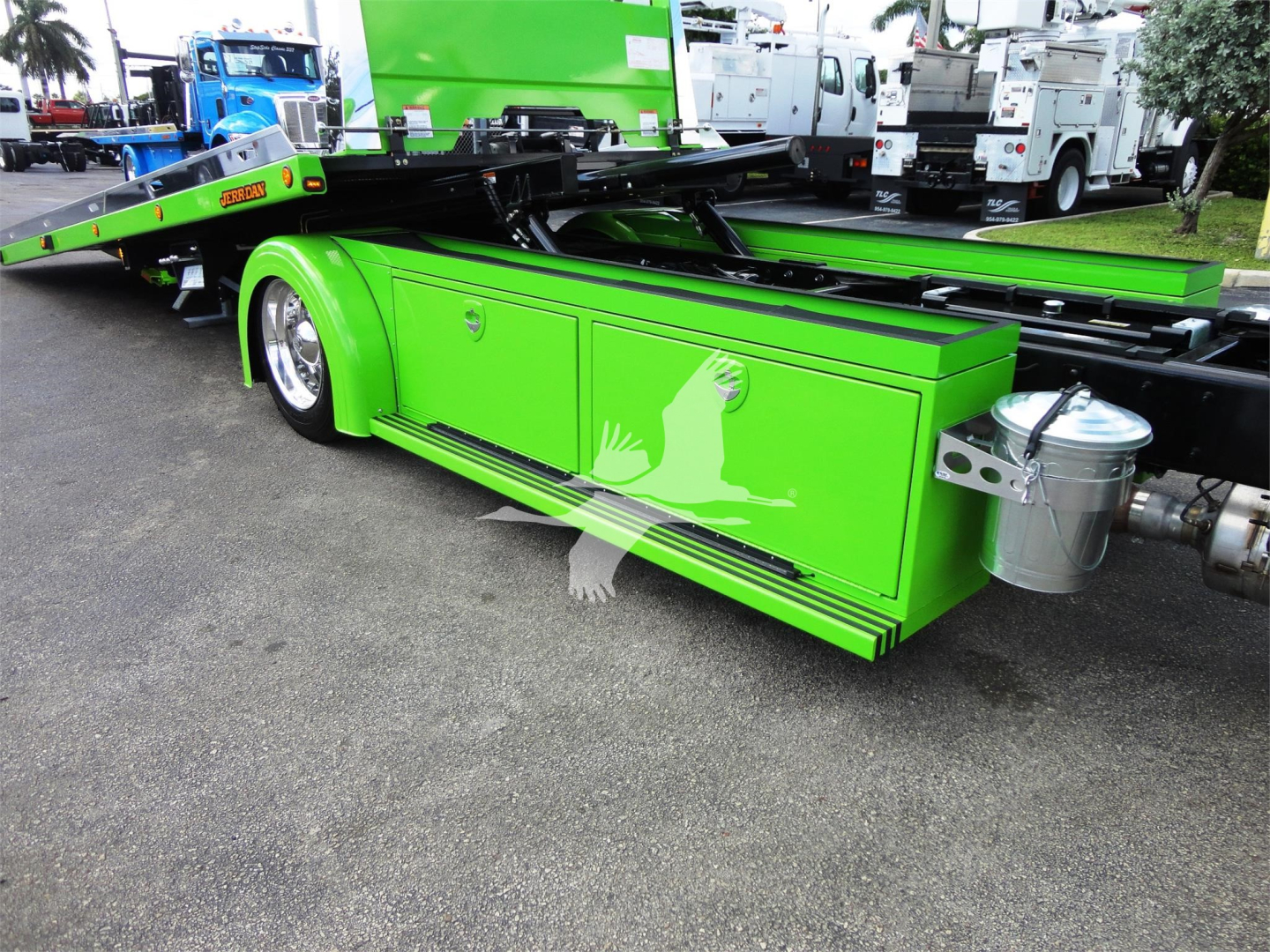 Green Peterbilt 337 rollback truck body side compartments with storage boxes and metallic tank, rear hitch area visible, other trucks in background.