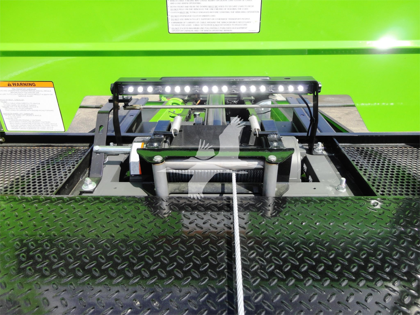 Trucks equipment bay with winch/lock mechanism and LED light bar on a green Peterbilt 337 rollback truck showing mounting hardware and diamond plate surface.