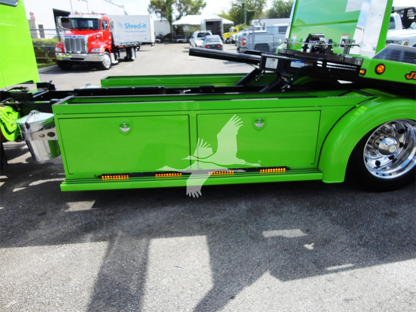 Green Peterbilt 337 rollback truck side panel with storage boxes and orange marker lights, part of a recreational equipment in a dealership lot.