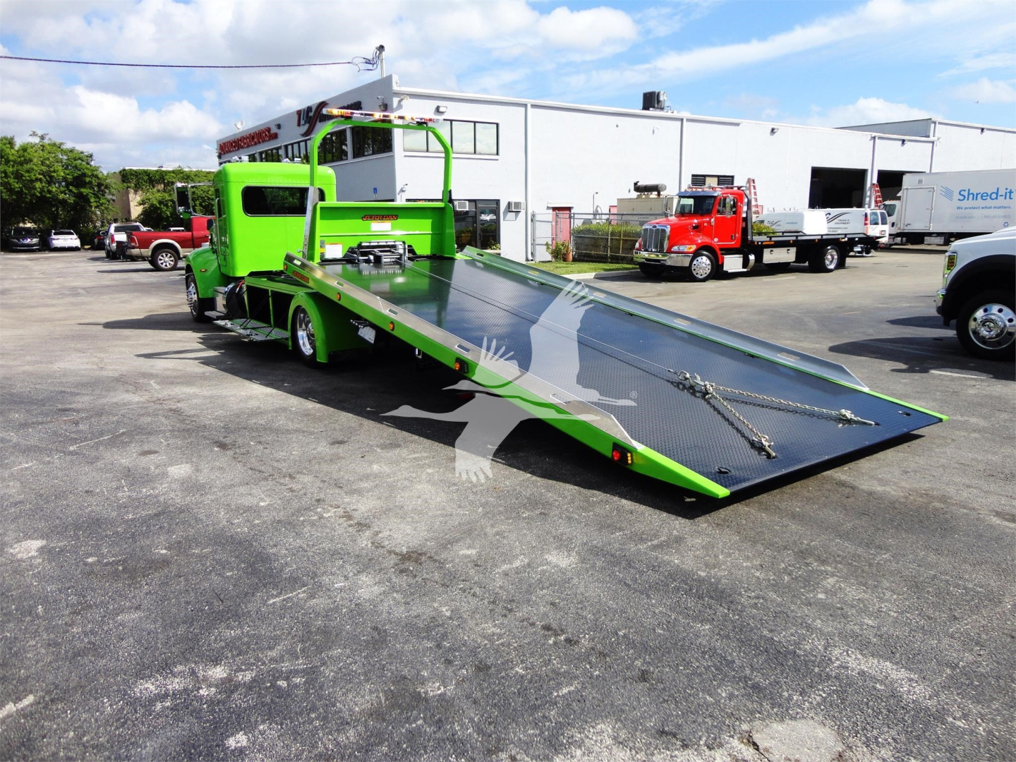 Green Peterbilt 337 rollback tow truck with a lowered steel ramp and cab, side view, in a dealership lot.