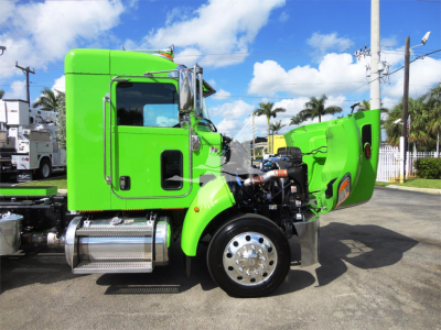 Peterbilt 337 truck in bright green with hood open showing engine bay and front wheel; rollback truck in background.