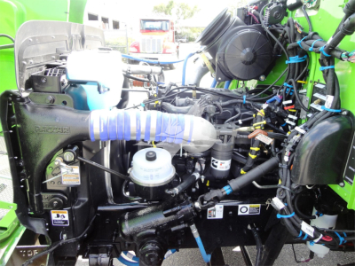 Peterbilt 337 engine bay showing cooling system, hoses, wiring, and components in a green truck; visible labels and reservoir caps.