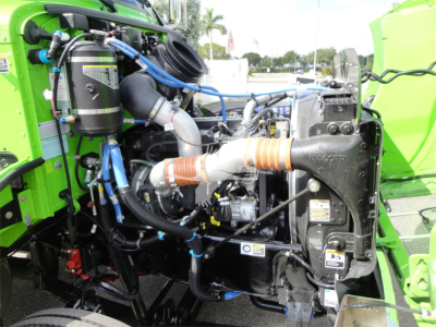 Peterbilt 337 engine bay with green cab, roll-back truck. Visible components include intercooler piping, air filter canister, hoses, wiring, and radiator support.