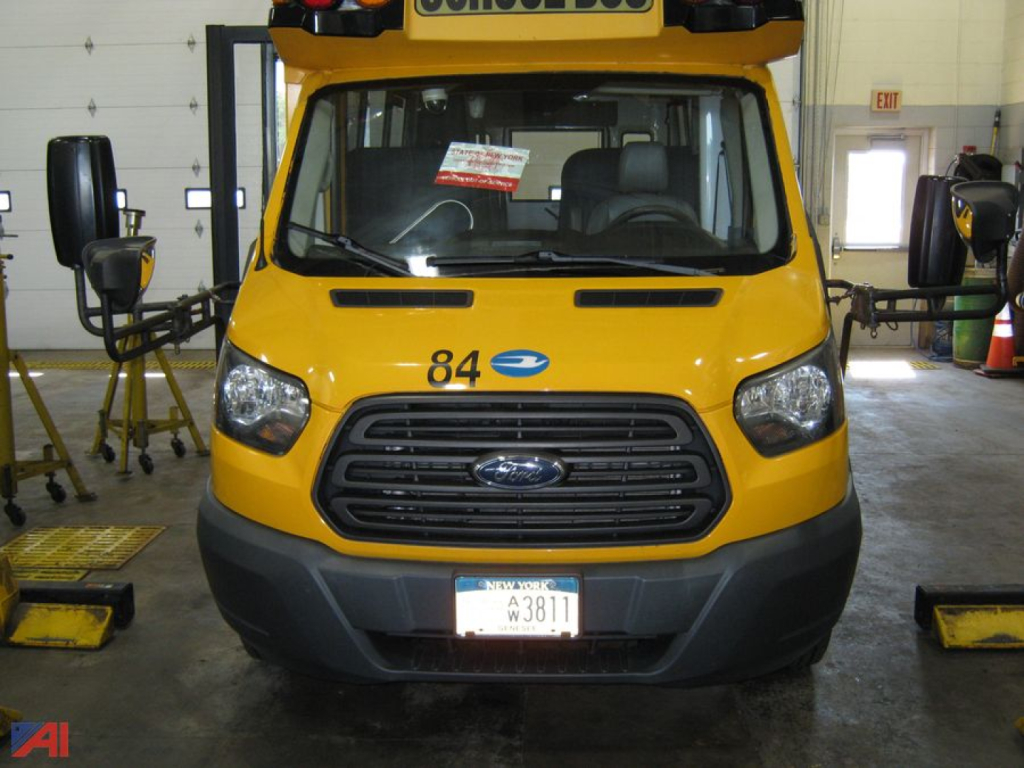 Front view of a yellow 2015 Ford 350HD Transit Bus with wheelchair lift, number 84, license plate visible, inside a service bay.