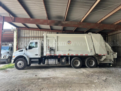 Kenworth T480 garbage truck side view showing cargo body and cab with wheel configuration, under a metal roof structure.