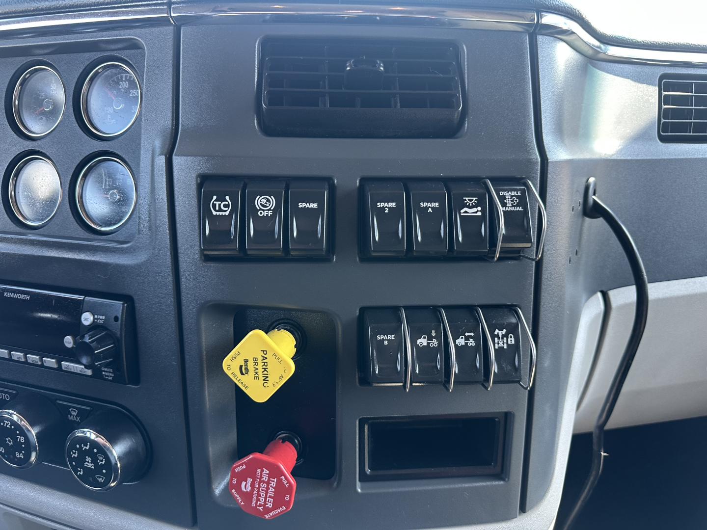 Peterbilt 579 dash cluster and switch panel with yellow and red handles showing controls and gauges.