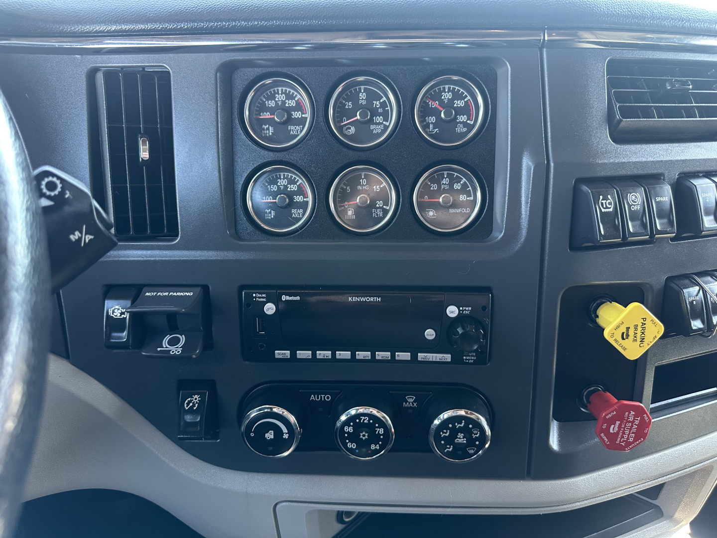 Dashboard of a Peterbilt truck showing multiple gauges and radio stack, control knobs, and a yellow knob in the center-right.