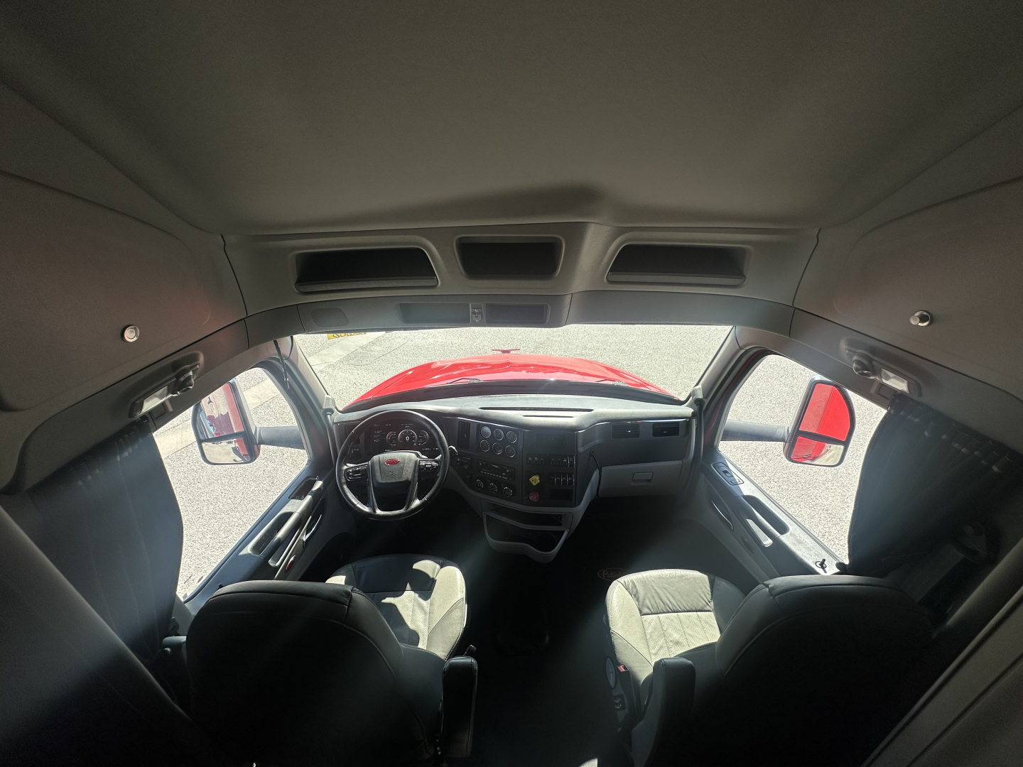 Peterbilt 579 interior cab view from front with dashboard and steering wheel; driver and passenger seats visible; red hood through windshield.