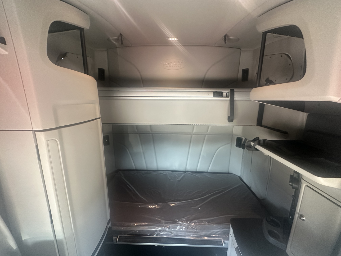 Peterbilt 579 sleeper cab interior showing cargo area with side cabinets and sleeping berth, light gray trim, storage shelves and steps.