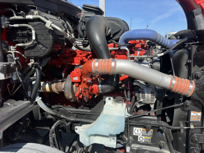 Peterbilt engine bay showing large orange diesel engine with blue intercooler piping and coolant reservoir labeled DACKER or Dacker, various hoses and components visible.