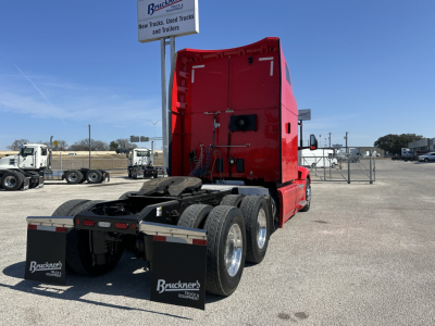 Peterbilt 579 diesel truck tractor rear view showing red sleeper cab and dual rear axles with fifth wheel, in a lot.