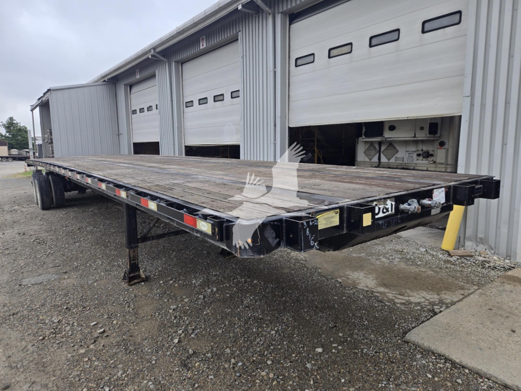 Flatbed trailer in a yard showing steel deck and undercarriage with two axles and circular hitch, stock number 7852.