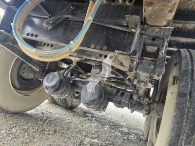 Rear undercarriage of a steel flatbed trailer showing hitch components, axles, suspension, and hoses.