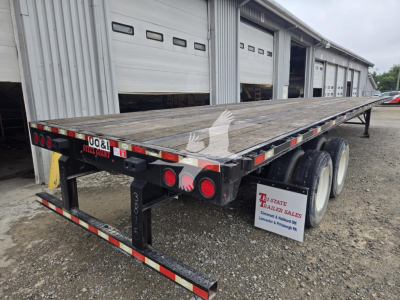 Flatbed trailer showing dual rear wheels and wooden deck with reflective tape and rear lights. Side and rear view in yard.