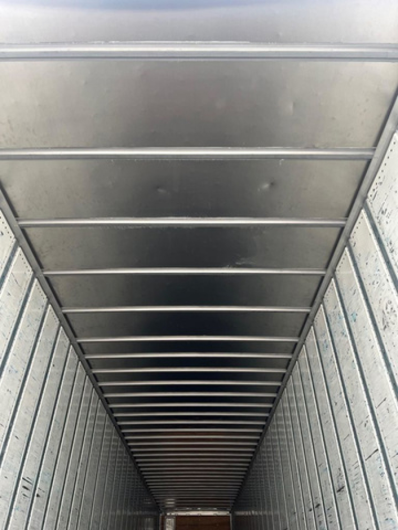 Interior of a trailer showing ribbed metal walls and ceiling with overhead lines, empty storage space.
